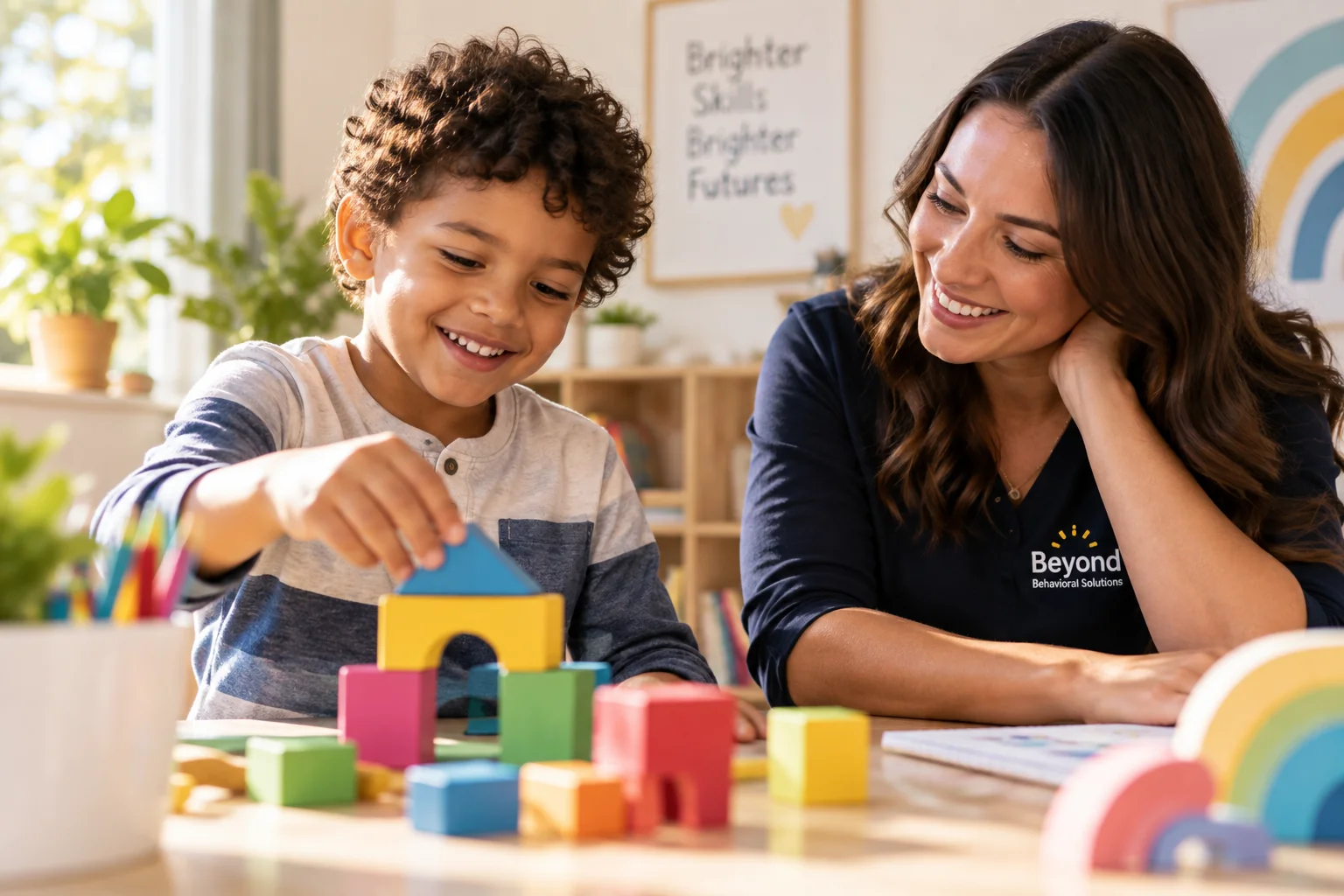A child stacks colorful blocks while a therapist sits alongside, smiling and supporting the activity.